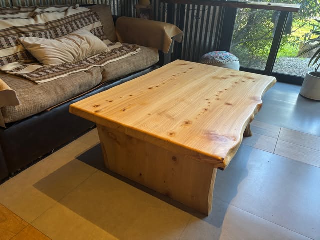 Mesa ratona de ciprés de 1,30 m con borde natural, junto a un sillón